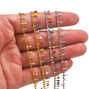 Colliers en acier inoxydable plaqué et perles en émail coloré présentés dans une main