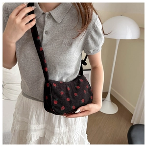 Close-up of black corduroy shoulder bag with red strawberry embroidery on model