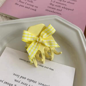 Detail of yellow hair claw clip with yellow and white checkered bow in cream tray