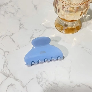 Detail of light blue acetate hair claw clip with gold logo on marble surface