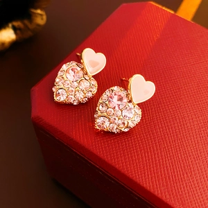 Close-up of pink heart earrings with sparkling crystals on a textured red gift box