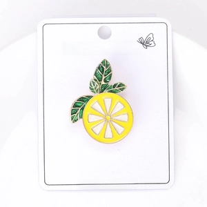 Detail of yellow enamel lemon brooch with green leaves on a white fashion jewelry card