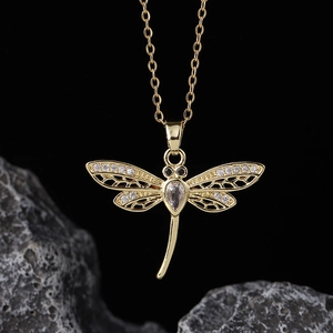Macro shot of gold dragonfly pendant necklace with sparkling cubic zirconia on dark stone