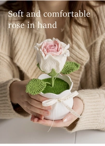 Close-up of handmade crochet rose in a white pot held by a person in a cozy sweater