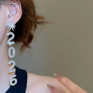 Détail de boucles d'oreilles argentées avec glands 2026 et clou fleur étincelant