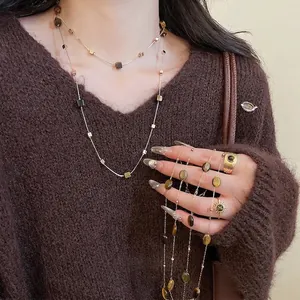 Layered gold necklaces and rings set with brown tiger eye stones on brown sweater