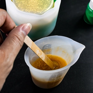 Close-up of 100ml silicone measuring cup with scale and liquid stirring for DIY resin