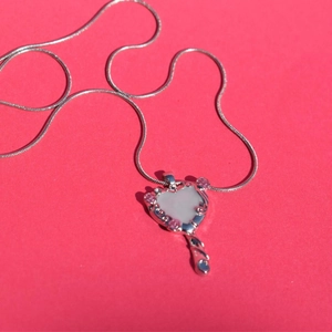 Close-up of a silver heart-shaped pendant with pink accents on a bright pink background