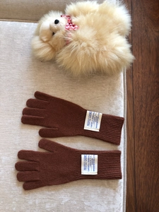 Detalle de guantes de lana marrón con etiqueta bordada sobre un cojín beige suave