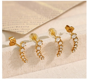 Macro shot of curved gold earrings with white zirconia stones on a linen display