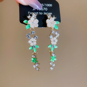Close-up of dangling flower earrings with white pearls and green leaf accents