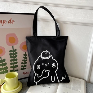 Detail of black canvas tote bag with white cat print placed on a book in a cozy setting