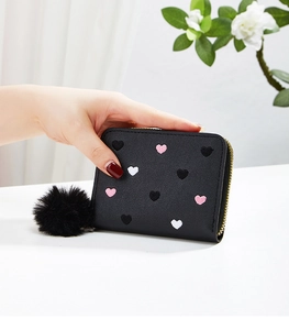 Detail of black wallet with embroidered hearts, gold zipper and black fur pompom pendant