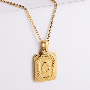 Detail of 18K gold plated rectangular pendant featuring embossed letter C with sunburst texture