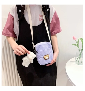 Detail of purple corduroy crossbody bag with brown bear embroidery and plush charm