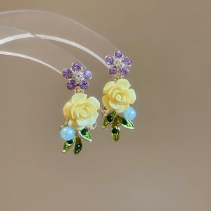 Detailed close-up of floral drop earrings with yellow rose, purple crystal, and blue bead