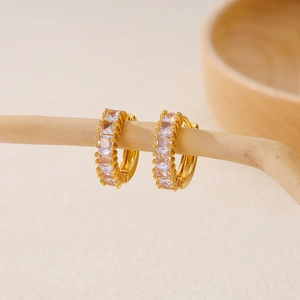 Detail of gold hoop earrings with rectangular zircons and milgrain edges on wood