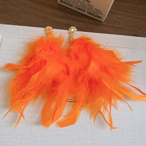 Dettaglio di orecchini bohémien con piume arancioni brillanti e perni in metallo dorato