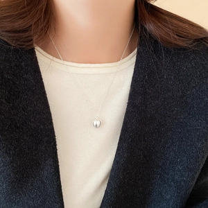 Detail view of a matte silver apple pendant necklace on a model wearing an elegant coat