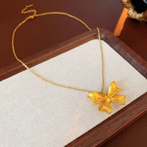 Detailed macro shot of a golden bow pendant necklace resting on a wood tray