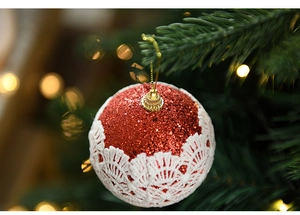 Close-up of 8cm red glitter Christmas ball with white lace hanging on a tree