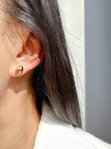 Close-up of minimalist polished gold bean stud earrings worn on a woman ear lobe