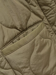 Close-up of olive green quilted jacket featuring wave stitching and side pocket detail