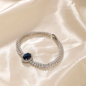 Macro detail of silver double-row diamond bracelet with oval blue gemstone on silk