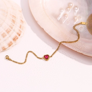 Macro shot of 18K gold Figaro chain bracelet with pink heart gemstone on seashell