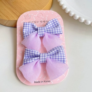 Détail de deux barrettes à nœuds violets à carreaux sur un plateau à perles blanches