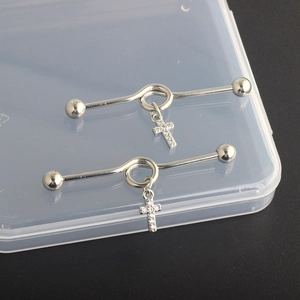 Close-up of silver industrial barbells with crystal-inlaid cross charms on dark base