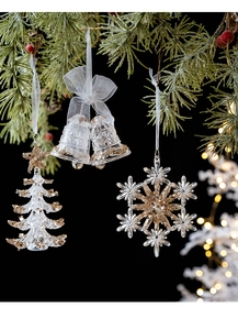 Close-up of clear acrylic snowflake and bell ornaments with gold glitter on pine branches