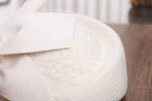Detailed shot of white wool pillbox hat with elegant mesh veil and bow accent