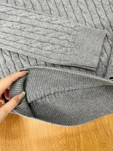 Macro detail of grey cable-knit texture and ribbed cuffs on a V-neck sweater