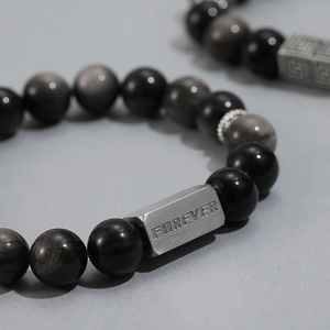 Macro detail of obsidian beaded bracelet featuring a silver metal charm with FOREVER engraving