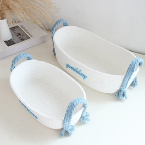 Close-up of woven cotton rope storage baskets with blue 'goodday' embroidery and tassels