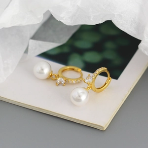 Macro shot of elegant gold earrings featuring sparkling zircon inlay and pearl drops