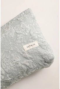 Close-up of sage green jacquard fabric with floral relief and H & R BAG woven label