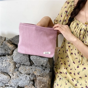 Detail of lavender corduroy cosmetic bag held by model against a white wall
