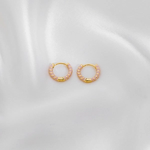 Detail of gold huggie hoop earrings featuring pink enamel spiral pattern on white silk