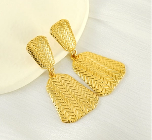 Close-up of gold geometric earrings with a 3D woven herringbone texture and dual links