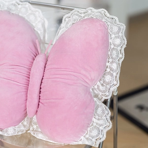 Close-up of pink butterfly plush pillow with white lace trim on a modern transparent chair