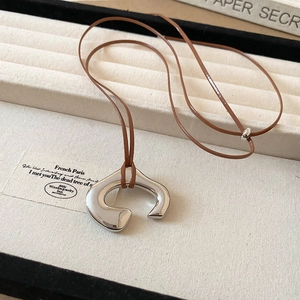 Macro shot of silver irregular C-shape pendant with brown cord on jewelry tray