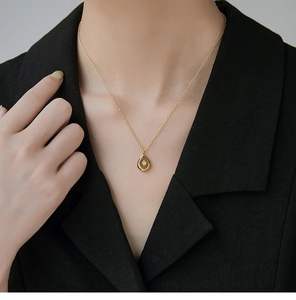 Detail view of a 18K gold plated drop pendant necklace on a black blazer model