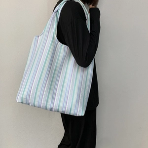 Vue latérale du sac fourre-tout rayé bleu et violet sur l'épaule du mannequin en toile