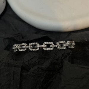 Macro detail of silver geometric links with pavé crystals on black paper background