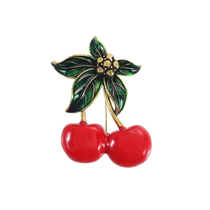 Charming red cherry brooch with green leaves and gold accents on a white background