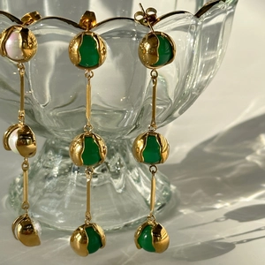 Close-up of vintage 18k gold earrings with green chalcedony and pearl on glass rim