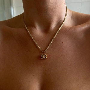 Close-up of golden number 98 pendant on twist rope chain worn by a female model