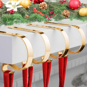 Close-up of four polished gold metal Christmas stocking hooks on a festive fireplace mantel
